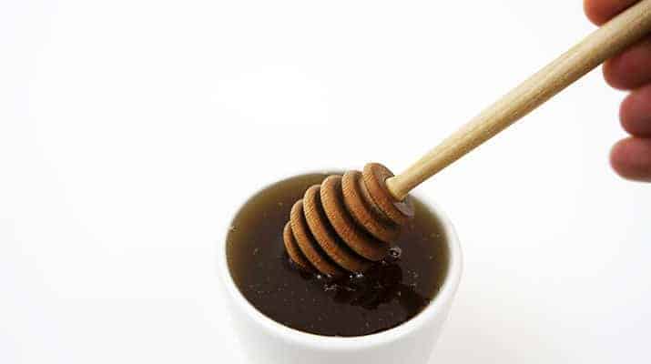 Dipping honey dipper into honey while holding stick