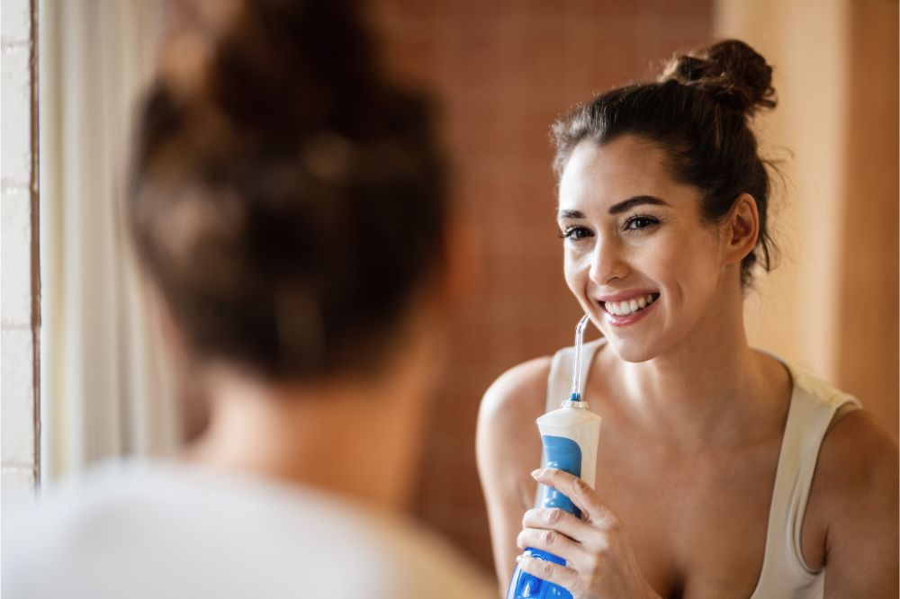Happy woman cleaning teeth with dental water flosser in the bathroom.